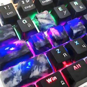 May include: Close-up of a mechanical keyboard with custom keycaps. The keycaps are black with a marbled, translucent design in shades of blue, purple, and white. The keyboard has LED backlighting in various colors, including red, green, and blue.