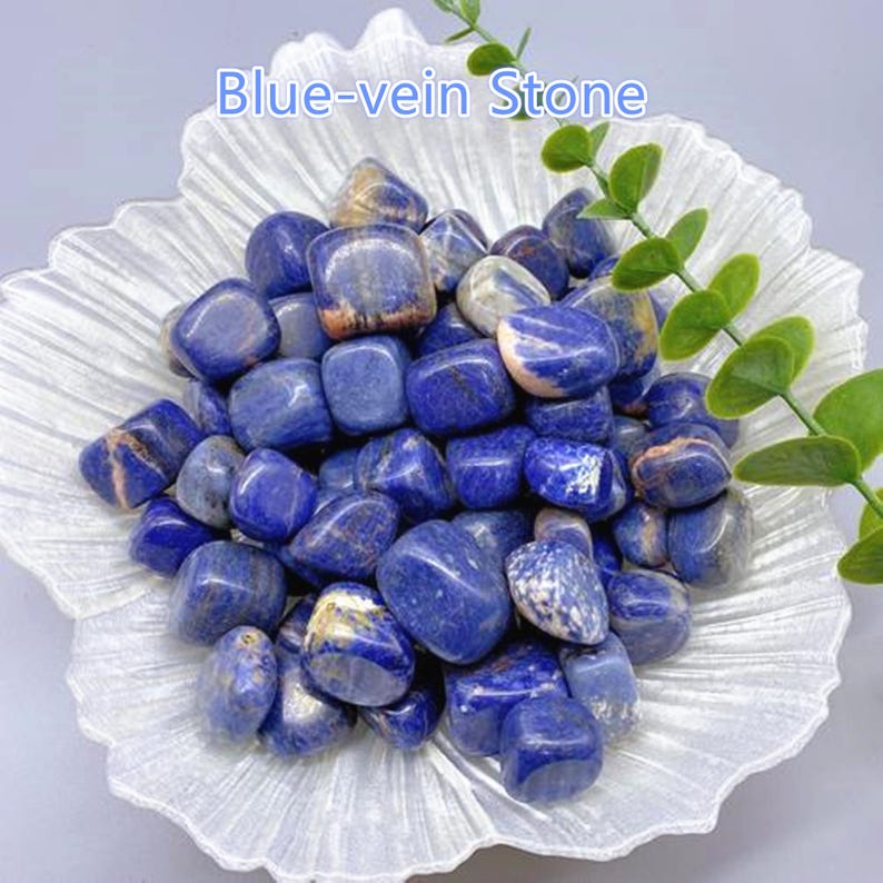 May include: A collection of polished blue-vein stones, with a mix of blue and white veining, displayed in a decorative, white, petal-shaped dish. The stones are smooth and rounded, with a glossy finish. The text "Blue-vein Stone" is visible.