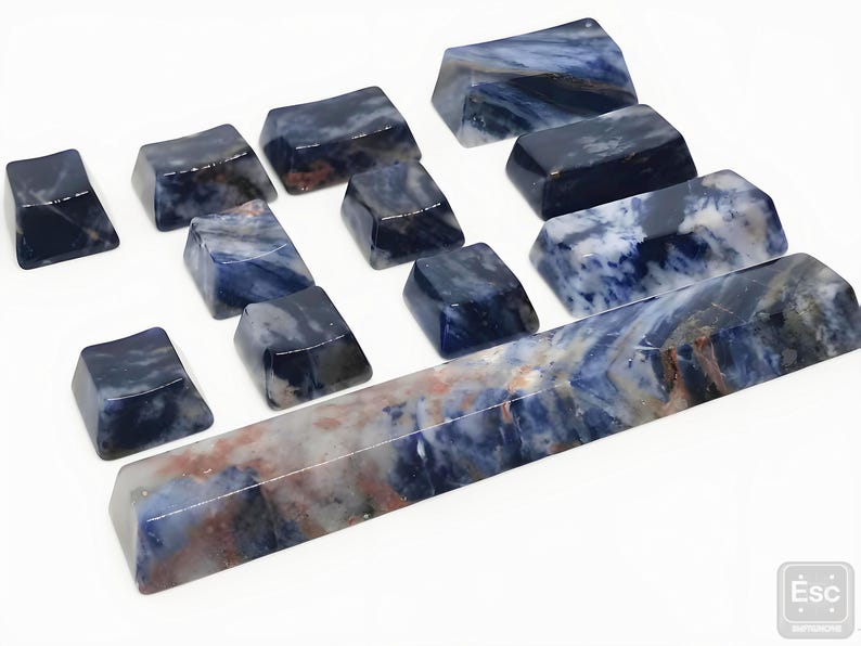 May include: A collection of polished, rectangular sodalite stones in various sizes. The stones display a mix of deep blue, white, and reddish-brown veining. The arrangement includes several small, square-shaped pieces and a long, rectangular piece.