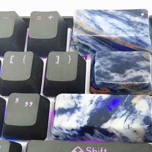 May include: Close-up of a mechanical keyboard with custom keycaps. The keycaps are made of a blue and white stone, with a marbled pattern. The standard black keycaps are also visible.