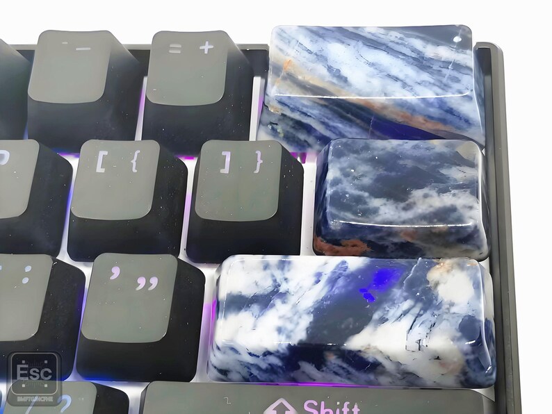 May include: Close-up of a mechanical keyboard with custom keycaps. The keycaps are made of a blue and white stone, with a marbled pattern. The standard black keycaps are also visible.