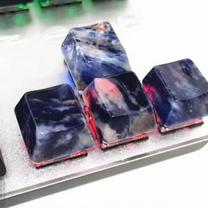 May include: Close-up of custom keyboard keycaps. The keycaps are made of a translucent material with a blue and white marbled pattern. The keycaps are lit from below with red and blue lights, creating a unique aesthetic.