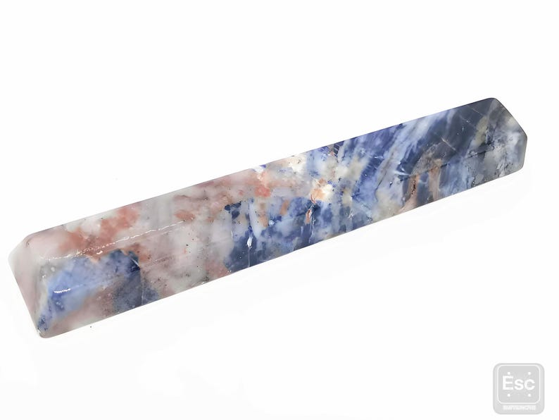 May include: A rectangular crystal wand with a polished finish. The wand features a blend of blue, white, and peach hues, creating a marbled effect. The crystal is a solid, elongated shape, perfect for display or use.