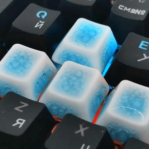 May include: Close-up of a mechanical keyboard with custom keycaps. The keycaps are white with a blue, ice-like design. The surrounding keys are black. The keyboard is lit with blue and orange lights.