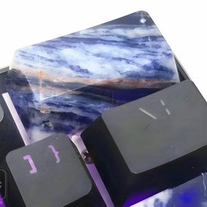 May include: Close-up of a mechanical keyboard with custom keycaps. The keycaps feature a blue and white marbled design, with some keys in black. The keyboard has a metallic frame and purple backlighting.