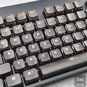 Puede incluir: Primer plano de un teclado mecánico con teclas de madera. Las teclas son de color marrón oscuro con letras blancas. El teclado tiene un marco negro e incluye teclas como "ALT" y "Esc".