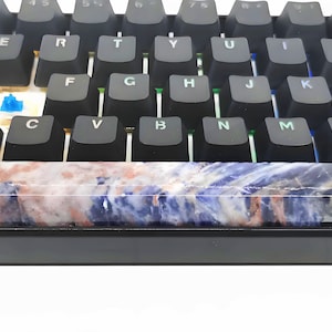May include: A close-up of a mechanical keyboard with black keycaps. The spacebar is a custom design with a marbled pattern in shades of blue, white, and red. The keyboard has blue and green LED lights.