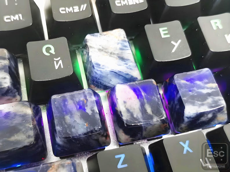 May include: Close-up of a mechanical keyboard with custom keycaps. The keycaps are made of a translucent material with a blue and white marbled pattern. The keyboard keys are black with white and blue lettering.