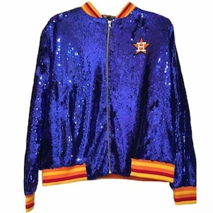 May include: A blue sequined bomber jacket with a zipper closure. The jacket features a colorful striped collar, cuffs, and waistband. An orange star with a letter "H" is on the chest.