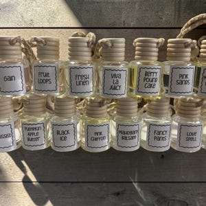 Può includere: Una collezione di piccoli flaconi in vetro per profumatori auto con tappi in legno e cordini. Ogni flacone presenta un'etichetta bianca con bordo smerlato e testo che include Gain, Fruit Loops, Fresh Linen, Viva La Juicy, Berry Pound Cake, Pink Sands, Mahogany Pumpkin, Narcissist, Pumpkin Apple Butter, Black Ice, Pink Chiffon, Mahogany Balsam, Fancy Pants, Love Spell e Mahogany Fierce.