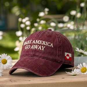 May include: A maroon baseball cap with the embroidered text "MAKE AMERICA GO AWAY" in white. The cap features a small flag patch on the side and a curved brim. The hat is sitting on a wooden surface.