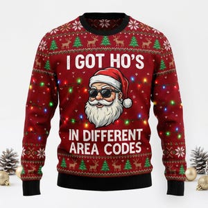 May include: A red long-sleeve crewneck sweater featuring a graphic of Santa Claus wearing sunglasses. The text I GOT HO'S IN DIFFERENT AREA CODES is printed in white. The sweater has a pattern of green Christmas trees, reindeer, and string lights.