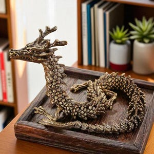 May include: A detailed bronze dragon sculpture with red eyes, resting on a dark wooden tray. The dragon features intricate scale and horn details. The sculpture is a decorative item, possibly for home decor or a collector's piece.