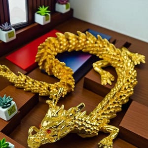 May include: A golden dragon figurine with intricate detailing, including scales and a red eye. The dragon is posed on a wooden surface, with a curved body and outstretched limbs. The figurine is a decorative item.