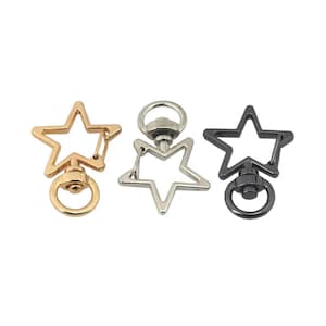 May include: Three star-shaped swivel clasps in gold, silver, and black. Each clasp features a star outline with a lobster claw clasp and a ring for attaching to a keychain or other accessories. The clasps are made of metal.