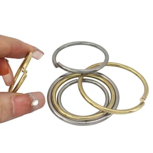 May include: A collection of metal key rings in gold and silver tones. One ring is being held open, while the others are interlocked. The rings are circular and appear to be made of a durable metal.