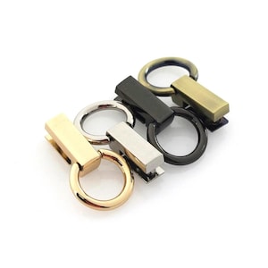 May include: An assortment of metal hardware pieces, including rings and rectangular bars, in various finishes. The colors include gold, silver, black, and bronze. These components are likely for bag making or other craft projects.