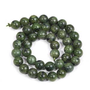 May include: A strand of round, green beads with dark speckles. The beads are strung together on a green string, creating a necklace or bracelet component. The beads have a polished, smooth surface.