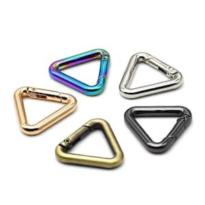 Puede incluir: Una colección de cinco mosquetones triangulares en varios acabados metálicos. Los colores incluyen iridiscente, plateado, dorado, latón antiguo y negro. Cada clip tiene una puerta con resorte para un cierre seguro.
