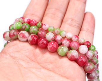 Peut inclure: Colliers de perles de pierres précieuses aux tons rouges, verts et blancs. Les perles sont rondes et semblent polies. Les perles sont tenues dans une main, mettant en valeur les couleurs et les textures des pierres.
