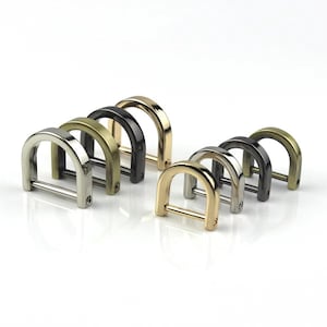 Könnte beinhalten: Eine Sammlung von D-Ringen in verschiedenen metallischen Ausführungen, darunter Silber, Gold, Schwarz und Antik-Messing. Diese Metallbeschläge sind in Reihen angeordnet und zeigen ihr gebogenes Design und die horizontale Stange.