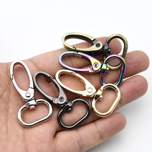 Puede incluir: Colección de cierres giratorios metálicos en varios colores, incluyendo plata, oro, negro y tonos arcoíris iridiscentes. Los cierres ovalados tienen una compuerta con resorte para una fijación segura. Ideal para manualidades o bolsos.