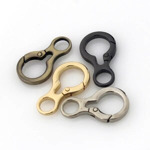 May include: Four metal swivel clasps in antique brass, gold, black, and silver. The clasps have a circular ring on one end and a swivel hook on the other, ideal for attaching to bags, keychains, or other accessories.