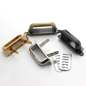 Könnte beinhalten: Eine Auswahl an Metall-Handtaschengriffen und -Verschlüssen in Gold-, Silber- und Schwarz-Ausführungen. Die Griffe haben eine rechteckige Basis mit einem gebogenen Griff. Einige Verschlüsse enthalten eine geschlitzte Metallplatte.