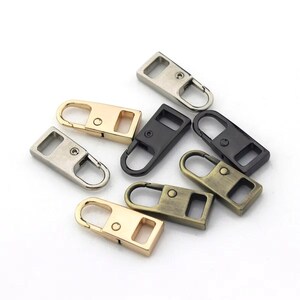 May include: A collection of metal zipper pulls in various colors, including gold, silver, black, and bronze. Each pull has a rectangular body with a loop for attachment and a small hole for the zipper slider.