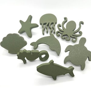May include: A collection of olive green wooden sea creature cutouts, including a starfish, jellyfish, octopus, dolphin, seahorse, shark, turtle, and seashell. These decorative shapes are ideal for nautical-themed crafts and decor.