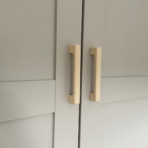 Könnte beinhalten: Nahaufnahme einer hellgrauen Schranktür mit zwei vertikalen, rechteckigen, goldfarbenen Griffen. Die Griffe sind auf der Tür zentriert und haben ein schlichtes, modernes Design. Die Schranktür hat eine eingelassene Platte.