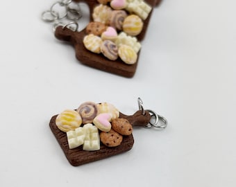 May include: A miniature wooden cutting board with a variety of colorful cookies and white chocolate pieces. The board is brown and has a wood grain texture. The cookies are arranged in a decorative pattern.