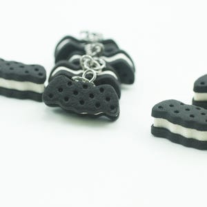 May include: A close-up of several black and white miniature cookies with a white filling. The cookies are arranged in a row and are connected by a silver chain.