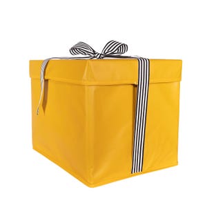 May include: A mustard yellow storage box with a black and white striped ribbon and bow. The box is square and has a lid. The ribbon is wrapped around the box and tied in a bow on top.
