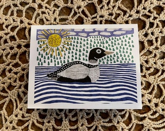 May include: A square art print featuring a stylized illustration of a loon swimming on blue water. The background includes a yellow sun, green trees, and a blue sky. The loon is black, white, and gray.