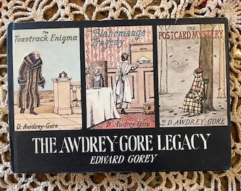 May include: A black and white book cover with the title "The Awdrey-Gore Legacy" by Edward Gorey. The cover features three illustrations from the book: "The Toastrack Enigma", "The Blancmange Tragedy", and "The Postcard Mystery".