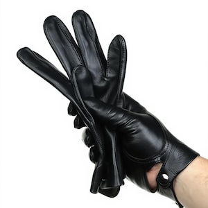 Könnte beinhalten: Ein Paar schwarze Lederhandschuhe. Die Handschuhe sind fingerlos mit einem Knopfverschluss am Handgelenk. Die Handschuhe sind aus glattem, glänzendem Leder gefertigt.