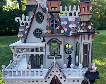 May include: A multi-story wooden dollhouse with a white, gray, and copper color scheme. The structure features intricate railings, a shingled roof, multiple windows, a front porch, and a doormat with the word Beware printed on it.