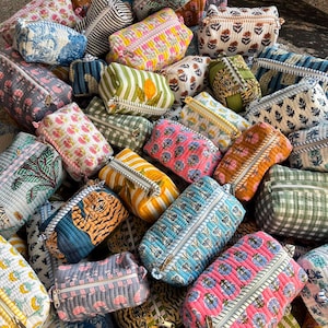 May include: A collection of rectangular quilted fabric pouches featuring various patterns including floral prints, tiger motifs, lemon illustrations, stripes, and gingham checks, each equipped with a white zipper closure along the top edge.