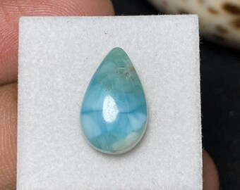 May include: A teardrop-shaped larimar gemstone, showcasing a blend of light blue and white hues. The polished stone is set against a white background, highlighting its natural patterns and textures. The gemstone is a popular choice for jewelry.