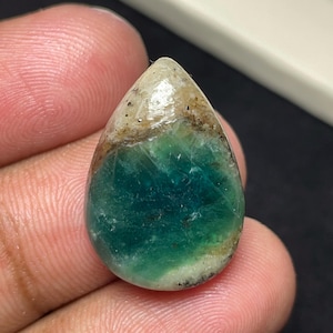 May include: A teardrop-shaped gemstone featuring a smooth, polished surface with a gradient of deep teal and green transitioning into a creamy beige and brown top section, displaying natural inclusions and a glossy, reflective finish throughout.