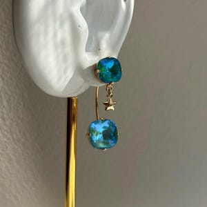 Pendientes artesanales chapados en oro de 24k con cristal Aurora en verde y azul turquesa. Diseño con doble cristal y diseño anverso. Incluyen un colgante tipo ear jacket y un pequeño dije de estrella.