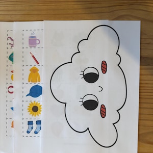 Puede incluir: Hojas de papel blanco con ilustraciones de dibujos animados. Una hoja presenta una cara de nube con ojos negros y detalles rojos. Otras hojas muestran una taza, un lápiz, una chaqueta, una gorra, un girasol y calcetines.