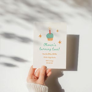 May include: A birthday invitation with a cupcake illustration and the text "Olivier's turning two!" in teal. The invitation also includes the date, time, and RSVP information. The design features star accents in orange.