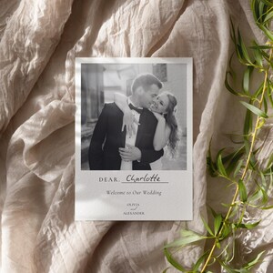 Könnte beinhalten: Eine rechteckige Hochzeitseinladungskarte mit einem schwarz-weiß Foto eines sich umarmenden Paares. Der Text lautet DEAR. Charlotte, Welcome to Our Wedding sowie OLIVIA AND ALEXANDER. Die Karte hat einen weißen Rand und ein klares Design.