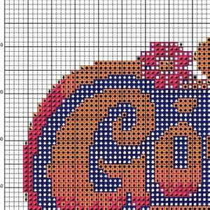 Puede incluir: Un patr&oacute;n de punto de cruz con un dise&ntilde;o estilizado en tonos naranja, rosa y azul marino. El patr&oacute;n incluye un motivo central en espiral y un borde, adecuado para proyectos de bordado. El dise&ntilde;o se muestra en una cuadr&iacute;cula.
