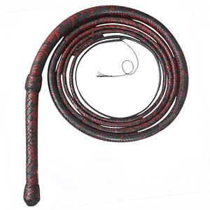 Puede incluir: Látigo de cuero trenzado en disposición enrollada. El látigo presenta un diseño bicolor con secciones rojas y negras alternas. El mango está tejido apretadamente y el látigo se estrecha hasta un punto fino.