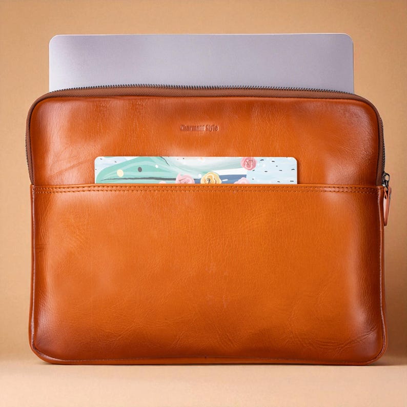 May include: A brown leather laptop sleeve with a zipper closure. The sleeve has a front pocket containing a colorful card. The laptop is partially visible inside the sleeve. The text "Charming Style" is visible on the front of the sleeve.