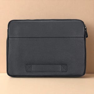 May include: A black leather laptop sleeve with a textured surface. The rectangular case has a zipper closure on the right side and a handle on the bottom. The sleeve is designed to protect a laptop.