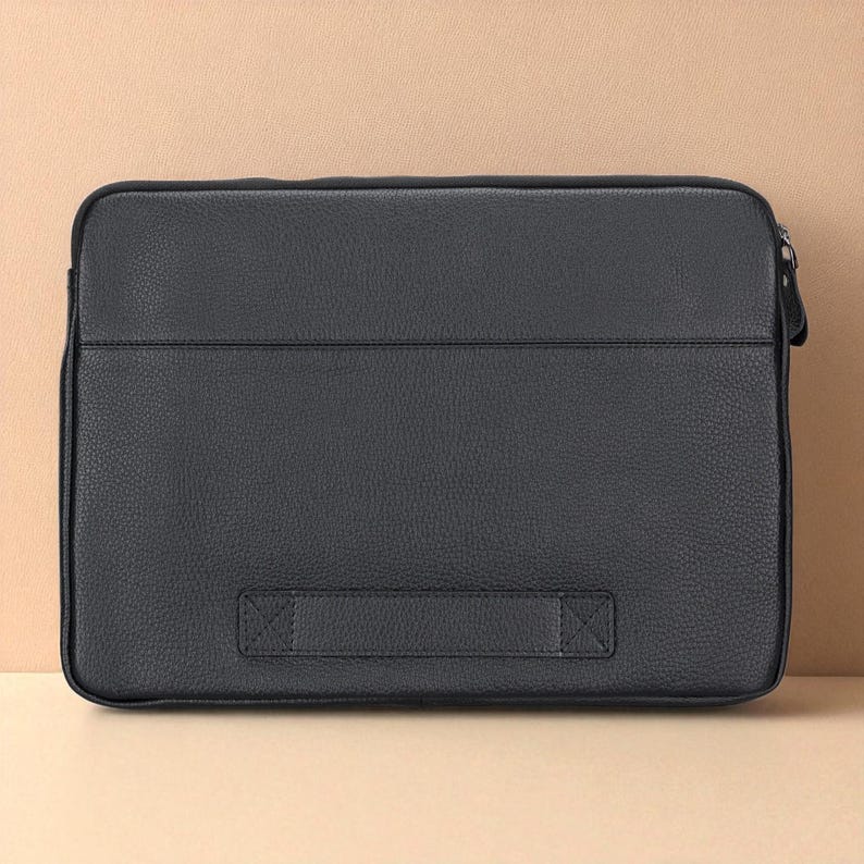 May include: A black leather laptop sleeve with a textured surface. The rectangular case has a zipper closure on the right side and a handle on the bottom. The sleeve is designed to protect a laptop.